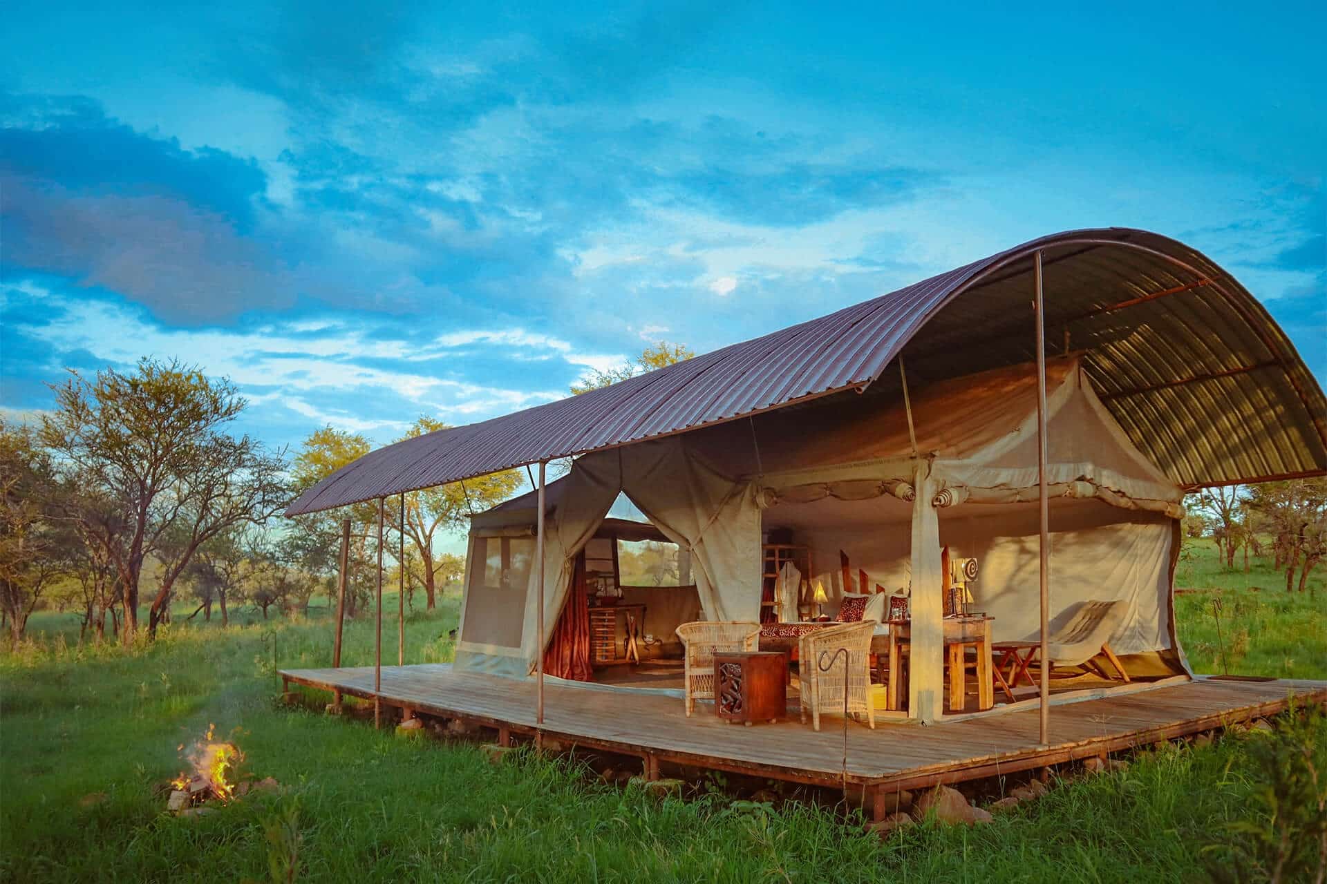 Curved-roof luxury safari tent on a raised deck with campfire at dusk, western Serengeti, Tanzania