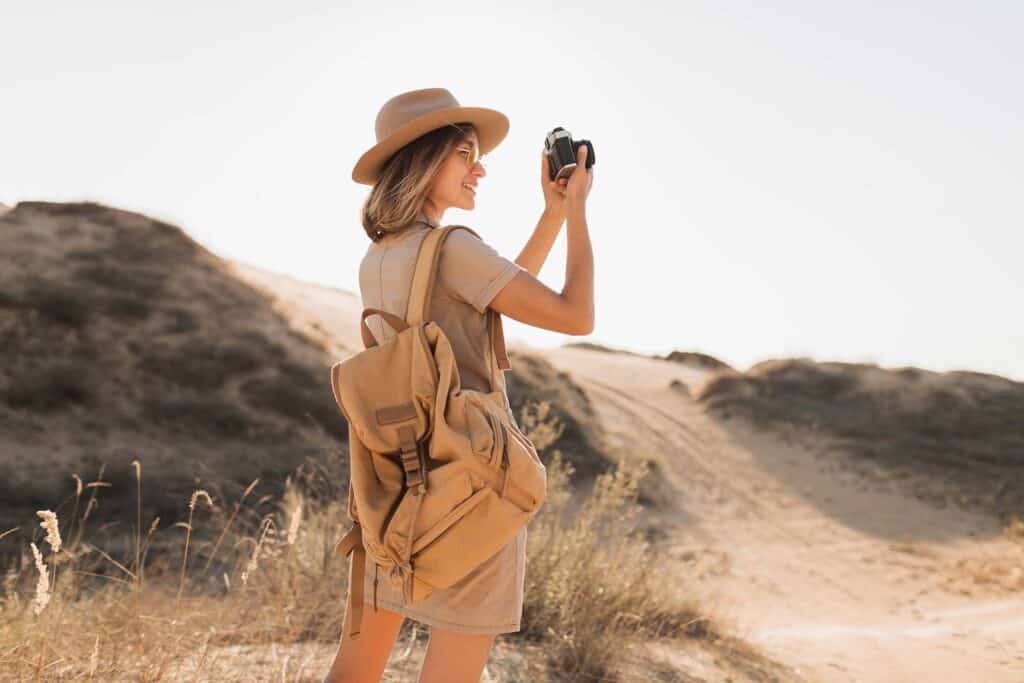 Woman in a safari hat and backpack taking photos with a camera on a Tanzania safari