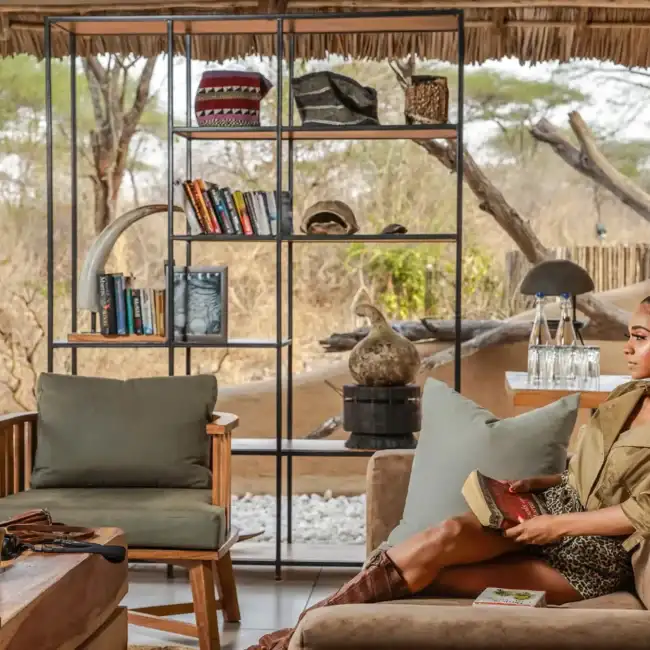 Guest relaxing with a book in the lounge of a luxury safari camp overlooking the bush, Tanzania
